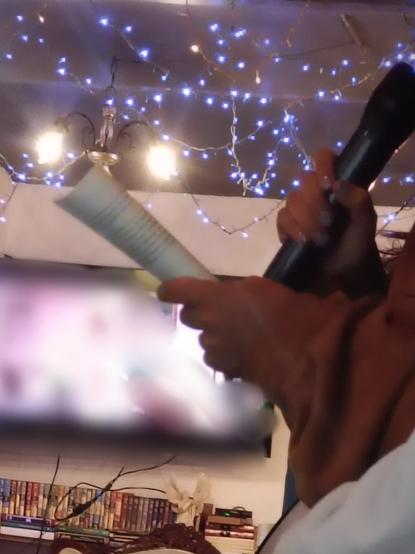 Manos sosteniendo un micrófono y un libro de poemas. De fondo, luces al interior de una cafetería.