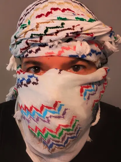 photo 1 - a person wearing a rainbow patterned keffiyeh wrapped around their head so only their brown eyes are visible.