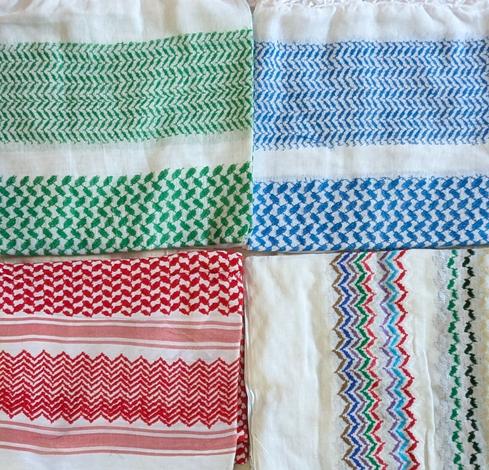 photo of four different keffiyeh neatly folded in a grid: green and white, blue and white, red and white, and a rainbow of colors and white