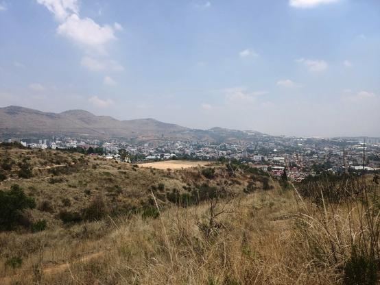 a photo of a village from a distant view where there is a sandy field and the population below the hills.