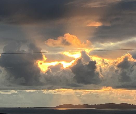The sun is setting behind white and gray poofy clouds, and a wide sunbeam is shining down onto the water like a spotlight, while another wide conical beam shines upward