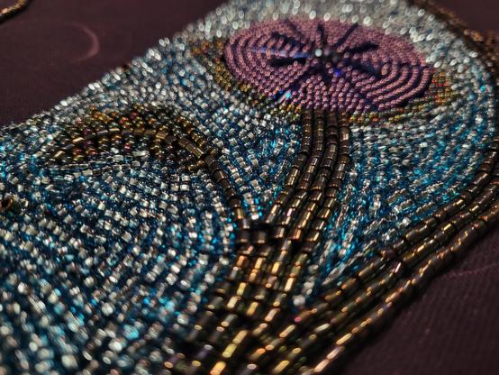 A closeup of the beadwork. The stem of a flower extends into the bluriness. The rows of tiny beads are near and orderly.