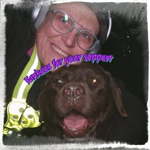 An edited selfie of Arwen, a chocolate brown Labrador with greying snout, and a person, me. I'm smiling at the camera and Arwen appears to be smiling too, as her mouth is open, showing some blep and teefs. A high-vis yellow safety harness is clearly visible in the snap. I'm wearing a black jacket under it. Also wearing blue-rimmed glasses, a red cap, and silver headphones. There is curved text over Arwen's head, partially on my face. The text is in pink, purple and teal, and it says "Fankoos for your support". There is a white cloudy frame around the snap.