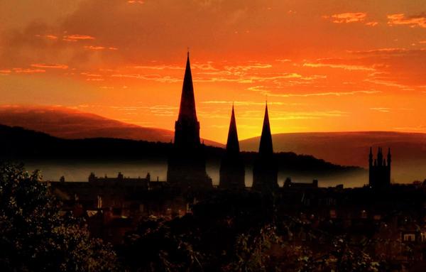 Image is of the skyline of Edinburgh in shadow as the sun rises behind with the Pentland Hills in the background
