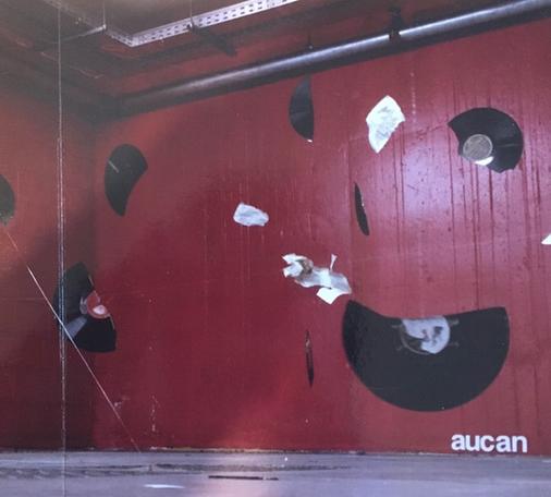 The cover art is a photo of a room or perhaps stage with red walls, with broken bits of vinyl records randomly placed, seemingly after the photo is taken (edited photo). The band's name is in small white font in the bottom right corner.