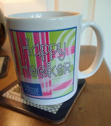 Mug of tea on a bedside cabinet with a green and pink background and the words happy hooker