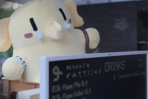 A mastodon plush sitting on a stack of beer crates. In front of it is a screen with a menu for the bar.