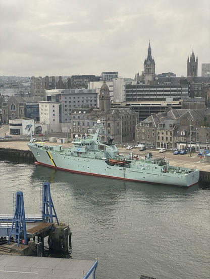 85 metre bottle green fishery support coastguard vessel ied up in Aberdeen harbour with much of the city centre in the background.