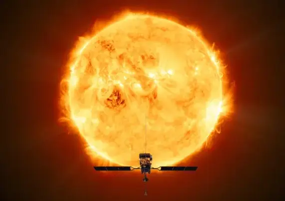 Bild einer in überwiegend gelber Farbe dargestellten Sonne. Die Strukturen auf der Sonnescheibe wirken sehr unruhig, am rand der Scheibe wölbt sich an vielen Stellen Material in großen leuchtenden Bögen über die Oberfläche hinaus und zurück. Das Bild muss in kurzwelligem Licht aufgenommen sein, da es Strukturen der inneren Korona zeigt. Neben den leuchtenden Bögen geht von der Sonnenscheibe geht ein orangerotes Hintergrundleuchten in alle Richtungen aus. Ganz am unteren Bildran ist die Silhouette einer Raumsonde zu sehen, deren ausladende Solarpanele nach rechts und links vom Raumfahrzeug abstehen. Nach oben und unten ragen jeweils Antennen hinaus.