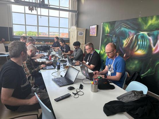 The unicorn room at Umbraco HQ in Odense, Denmark. A long table is surrounded by a group of friendly Umbraco community folks on their laptops, deep in thought as they hack their way into the Scummy Bar! ☠️