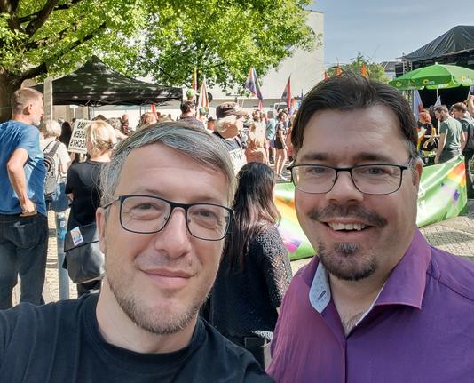 Helge und ich vor dem Landtag. Bunte Fahnen, viele Menschen, bestes Wetter.