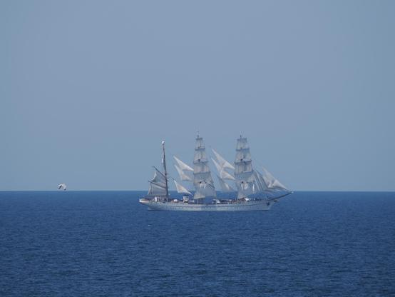 Ein weißes Segelschiff mit drei Masten unter vollen Segeln auf dem Meer.