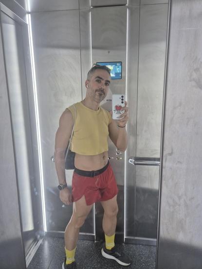 Selfie en el ascensor. Camiseta amarilla crop top sin mangas. Pantalón corto muy corto rojo.  Calcetines amarillos. Eyeliner y gafas de sol. Al orgullo se va sin pedir permiso ni perdón tan mamarracho como uno quiera.