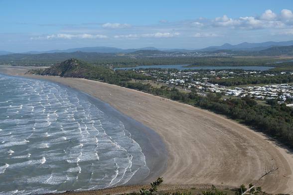A large bay with a large expanse of flat sand. There is some sort of wind powered vehicle race taking place on the sand. There are mountains in the distance.