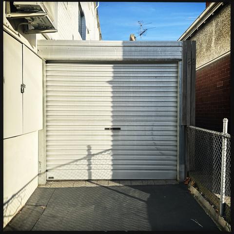 A white, corrugated garage door, right half in shadow and left half in wintry morning sun. A blue sky is in the background at the top.