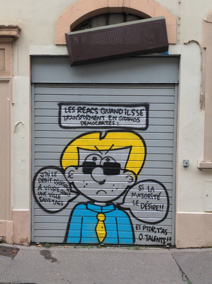 Sur un rideau métallique gris, titré "Les réacs quand ils se transforment en grands démocrates :", le personnage de Tapas, bonhomme BD blanc à gros nez, cheveux jaunes et haut bleu, ici bien peigné, avec des lunettes de soleil et une cravate jaune, dit : "J'ai le droit d'aspirer à vivre dans une ville sans tags", "si la majorité le désire !!" et "Et PTDR, t'as 0 talents !!".