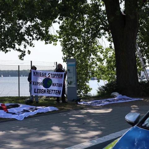 Foto: 2 Trasnpis liegen auf dem Boden, eine wird hochgehalten: "Kriege stoppen. Klima, Natur, Leben retten"