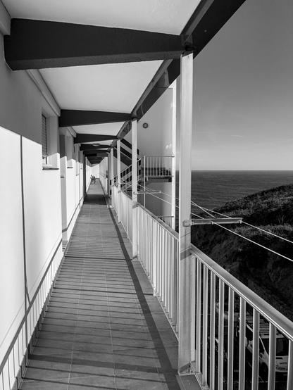 Vertical black and white image of a long narrow exterior hallway overlooking the Bay of Biscay in Bakio, northern Spain, which is in the heart of Basque country.