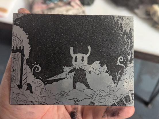 Plaque de gtavure encrée on voir bien le dessin 
le dessin représente le personnage de hollow knight qui tient son arme. Il est entouré de végétation de cailloux et d'une serre
