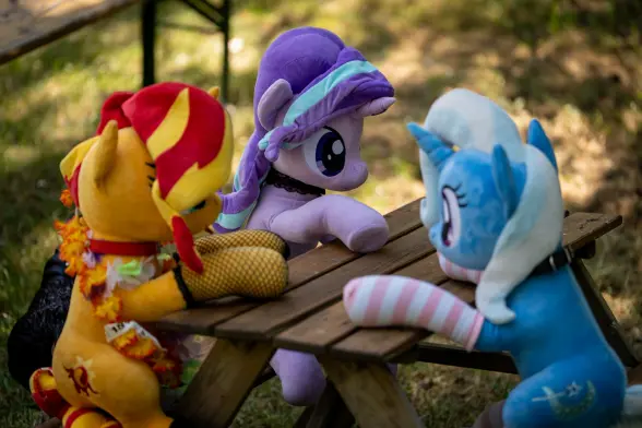 Sunset, Trixie and Starlight plushies sitting on a small bench table.