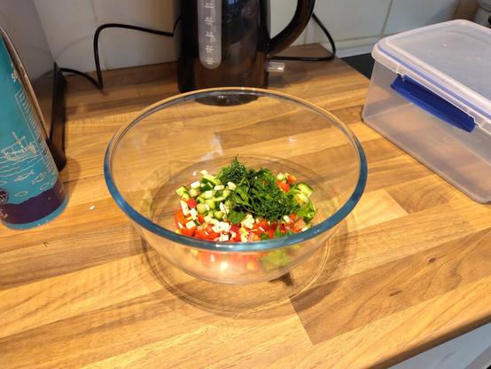 Chopped vegetables and herbs in a glass bowl.