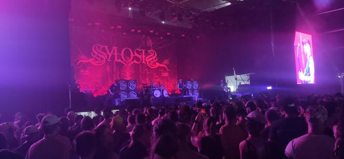 Sylosis in de Marquee op Graspop 2025. Achter de band is het rood verlicht en staat hun logo. Op de voorgrond staat publiek.
