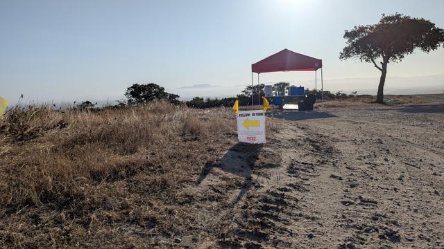 Sun shade with table and water on it. Small sign in the foreground with arrow telling runners which way to go
