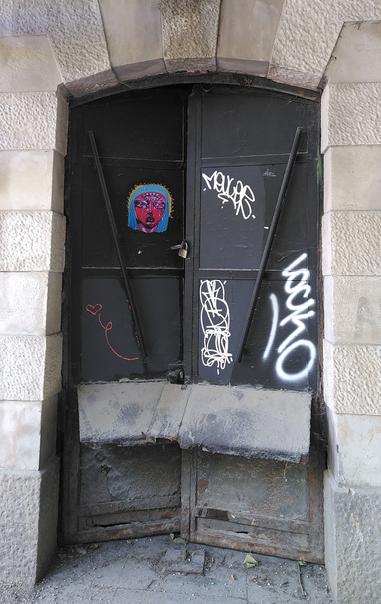 Porte métallique sombre et poussiéreuse, avec des graffitis blancs et une tête de femme rose avec trois yeux et des cheveux bleus