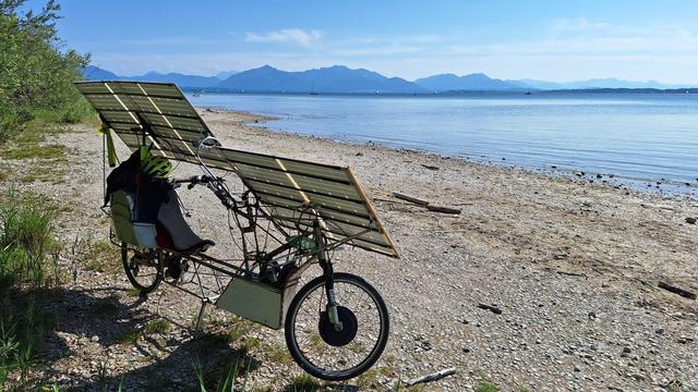 Solar recumbent bicycle parked at beach at the shore of the large lake. Mountains on the distant horizon.
