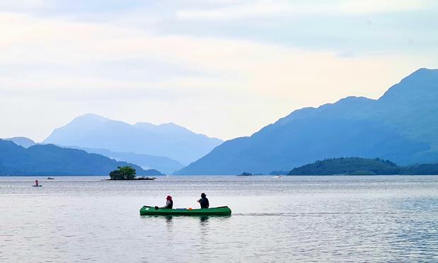 Two people in a canoe on a calm Scottish loch with misty mountains in the distance.