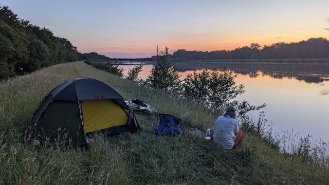 Schlafplatz für die 2te Nacht. Im Bild:
Zelt mit luftleeren Packraft im Hintergrund die Donau mit Spiegelung.