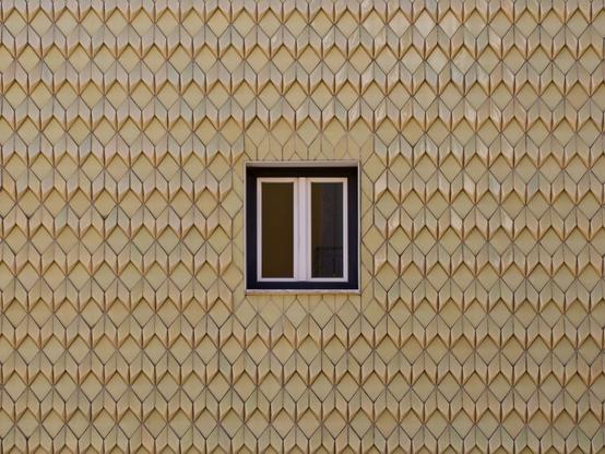 A wall of geometric, ceramic tiles on a home in Lisbon, Portugal. The only thing breaking the pattern is a two-paned window in the dead center of the image.