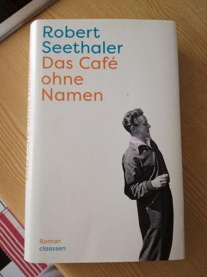 Weißes Buchcover von 'Das Café ohne Namen' von Robert Seethaler mit einem schwarz-weißen Foto eines Mannes in nach hinten gelehnter, seitlicher Haltung