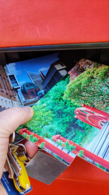 Set of different photo postcards almost dropped into a red/orange mailbox.