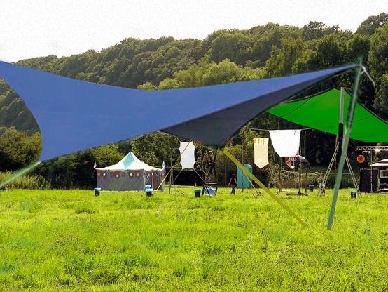 Eine grüne Wiese. Im Hintergrund sind Bäume.
Es sind für ein kleines Festival Sonnenschutz und Sonnensegel in verschiedene Formen und Farben aufgebaut worden