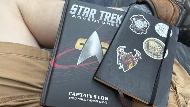 The Star Trek Captain’s Log rulebook and a notebook with geeky stickers on it.