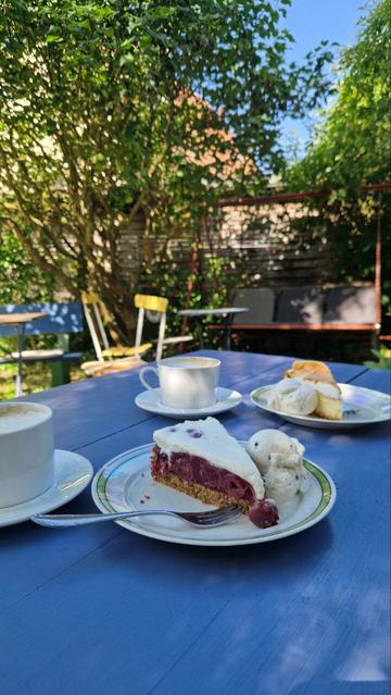 Zwei Stück Kuchen und zwei Kaffeetassen auf einem blauen Tisch mit sommerlichem Licht und Schatten.