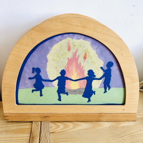 Wooden “De Noest” lamp with a handmade silhouette of four children dancing around a fire
