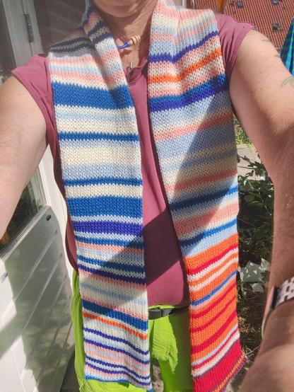 Selfie of me wearing a scarf in the climate stripe colours of Rotterdam. Due to the heat, I am wearing a tank top and shockingly bright green shorts.