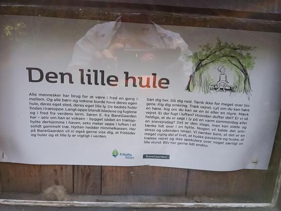 Skilt med Den Lille Hule

Første halvdel 
Alle mennesker har brug for at være i fred en gang i mellem. Og alle børn og voksne burde have deres egen hule, deres eget sted, deres eget lille ly. De bedste huler findes i trætoppe. Langt oppe blandt bladene og fuglene og i fred fra verdens larm. Søren E. fra BaneGaarden har selv om han er voksen - bygget sådan en trætop-hytte derhjemme i haven, seks meter oppe i luften i et solidt gammelt træ. Hytten hedder Himmelkassen. Her på BaneGaarden vil vi også gerne vise dig, at fristeder og huler og et lille ly er vigtigt i verden.

Anden del 
Sæt dig her. Slå dig ned. Tænk ikke for meget over tin-gene. Kig dig omkring. Træk vejret. Lyt om du kan høre en høne. Kig om du kan se en bi eller en myre. Mærk vejret. Er der fugt i luften? Hvordan dufter det? Er vi så heldige, at du er søgt i ly på en varm sommerdag eller en snevejrsdag? Det er den slags, man kan sidde og tænke lidt over i en hytte. Nogen vil kalde det anti-stress og udendørs terapi. Vi tænker bare, at det er en meget vigtig del af livet, at huske pauserne og huske, at trække vejret og ikke spekulere over noget særligt en lille stund. Bliv her gerne lidt endnu.