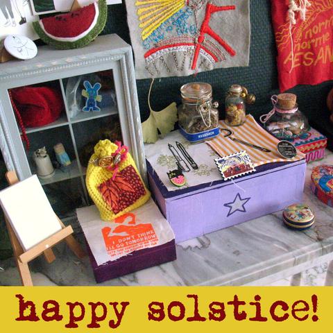 Zooming in on part of my Summer Solstice altar with a yellow spell bag, anti-work and pro-creativity patches, a postal stamp pin, a ginkgo leaf, little colourful boxes, and spell jars. Text undrneath says: Happy Solstice!