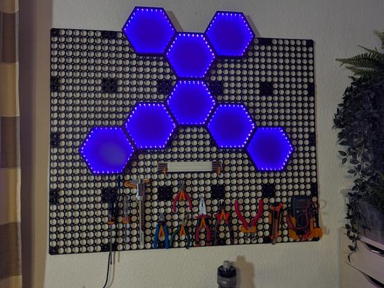 Eine Nahaufnahme des fertigen Multiboards. Daran hängen nun 8 blau beleuchtete Hexfelder, die eine Art "X" bilden. Darunter hängen diverse Werkzeuge, wie Schraubendreher, Meßschieber, Zangen, Cutter-Messer und ein Multimeter.