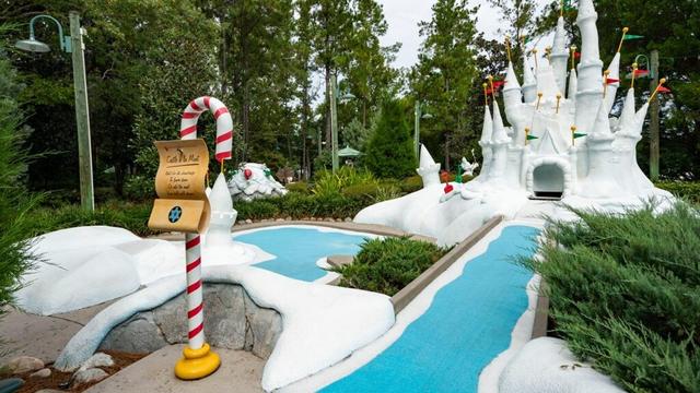 A whimsical Winter Summerland Mini Golf course with a snowy white castle, candy cane sign, and blue water paths.