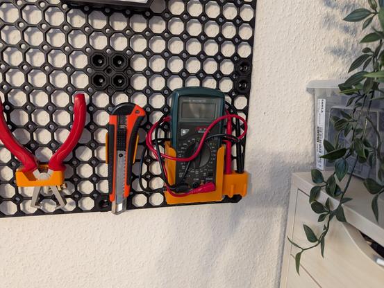 Eine Nahaufnahme der rechten unteren Ecke meines Multiboards. Von links nach rechts zu sehen: eine Zange zum abisoloeren von Kabeln, ein Cutter-Messer vom Baumarkt und ein Multimeter mit rotem und schwarzem Kabel und Messsonden. Rechts neben dem Board sind noch ein paar Pflanzen zu sehen.