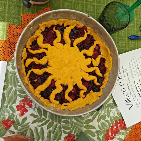A pie from blueberries and raspberrirs. The pie crust is dyed yellow with saffron, and forms a sun with wavy rays.