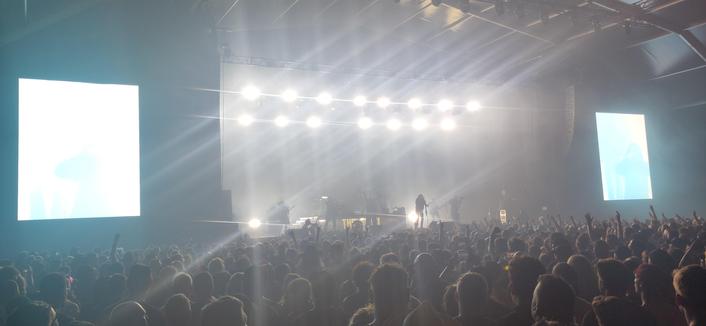 The Hu in de Marquee op Graspop 25. Er branden witte podiumlampen boven ze. Hun logo op de achtergrond is door de lampen (bijna) niet te zien. Op de voorgrond staat publiek.