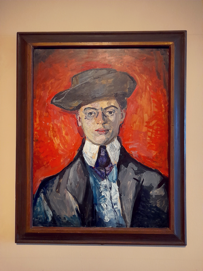 A painting hanging on a white wall. The painting is a portrait of a man in a suit wearing a hat. The background is bright red.