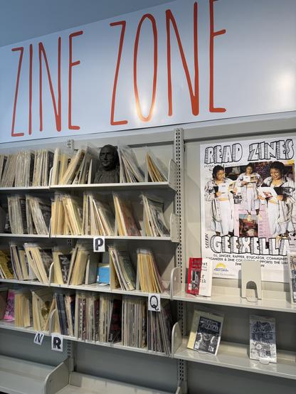A display titled "ZINE ZONE" shows shelves filled with various zines organized by letters. A bust of a person is visible, along with a prominent poster encouraging readers to explore zines.