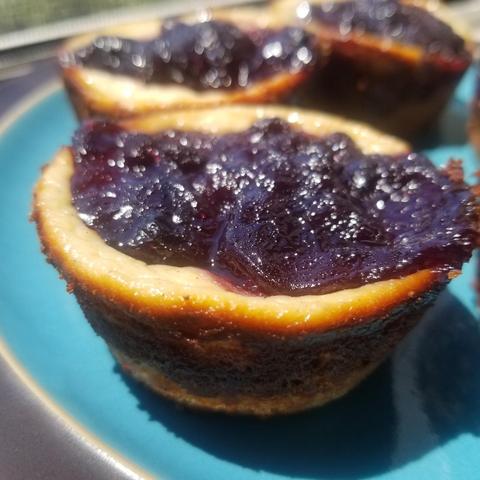 Photo of a turquoise plate of beautiful blueberry tarts, with one cut open to show the delicious center.