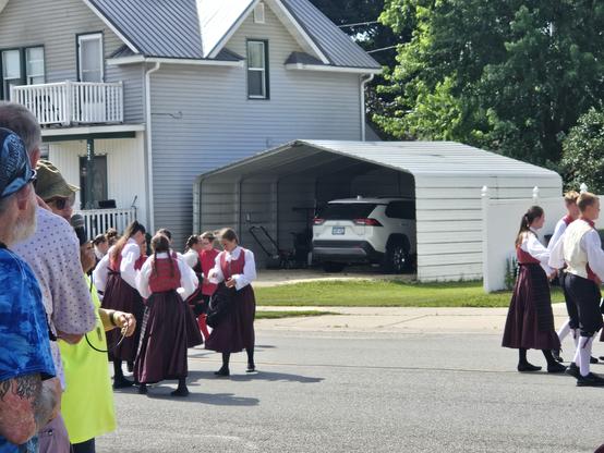 Nordic dancers in traditional costumes of red and white on an asphalt street.
